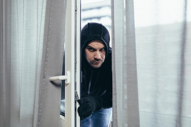 Ladro maschio in vestiti neri che prova a rompere la serratura della porta in casa