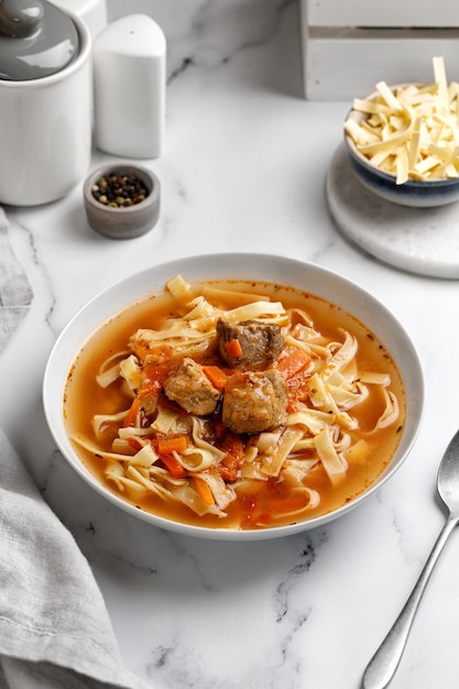 Lagman. La zuppa nazionale uzbeka con tagliatelle e pezzi di carne, verdure fritte. Chiudere la zuppa. Piatto bianco e fondo bianco