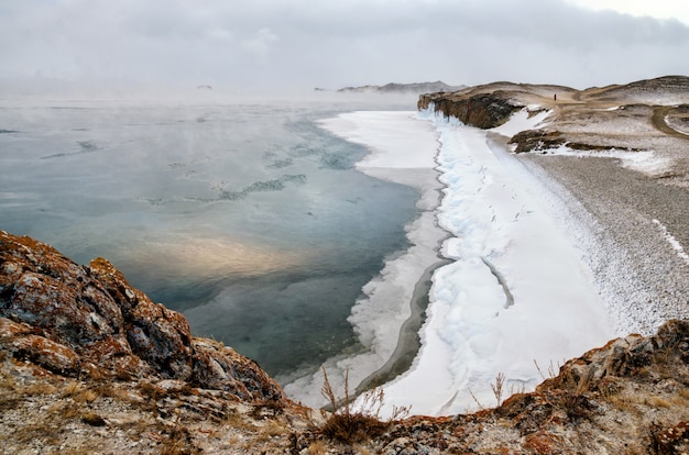 Lago Baikal e roccia nel freddo di dicembre. Tempo di congelamento. Lastroni di ghiaccio sta nuotando sull'acqua