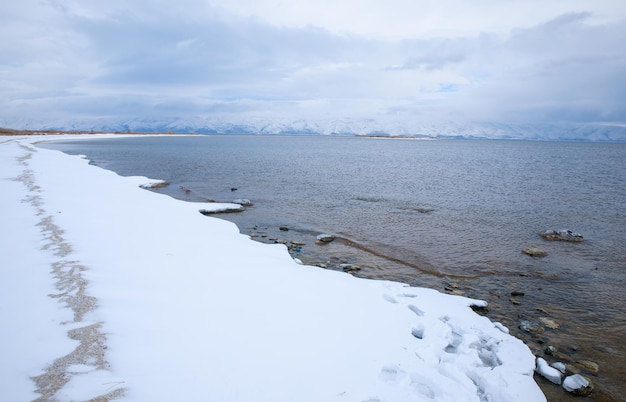 Lago con spiaggia innevata e montagna