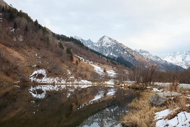 Lago di montagna invernale nella neve sullo sfondo dello stagno del paesaggio montano con ghiaccio sull'acqua