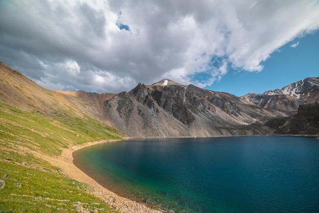 Lago di montagna profondo di colore blu fantasma tra alte montagne con picco appuntito in condizioni meteorologiche variabili Splendida vista spettacolare sul lago di montagna blu profondo tra rocce affilate illuminate dal sole sotto il cielo nuvoloso