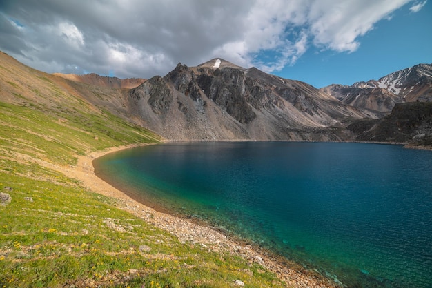 Lago di montagna profondo di colore blu fantasma tra alte montagne con picco appuntito in condizioni meteorologiche variabili Splendida vista spettacolare sul lago di montagna blu profondo tra rocce affilate illuminate dal sole sotto il cielo nuvoloso