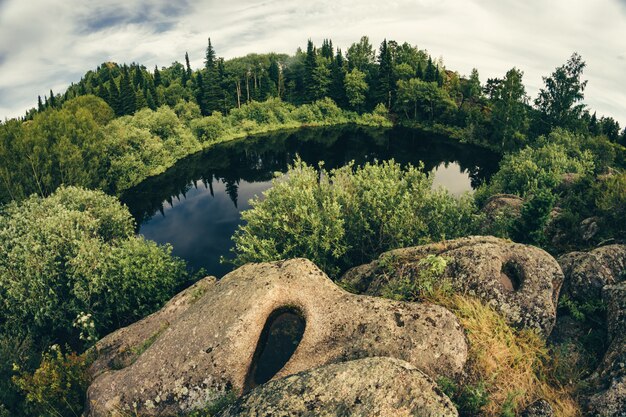 Lago in cima alla collina, circondato da rocce e boschetti, catturato dall'obiettivo fisheye.