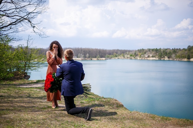 Lago nella foresta: un uomo ha fatto una sorpresa alla sua ragazza, le mette un anello al dito, una dichiarazione d'amore e un'offerta di matrimonio. Ragazza con un sorriso sul viso e un mazzo di rose rosse