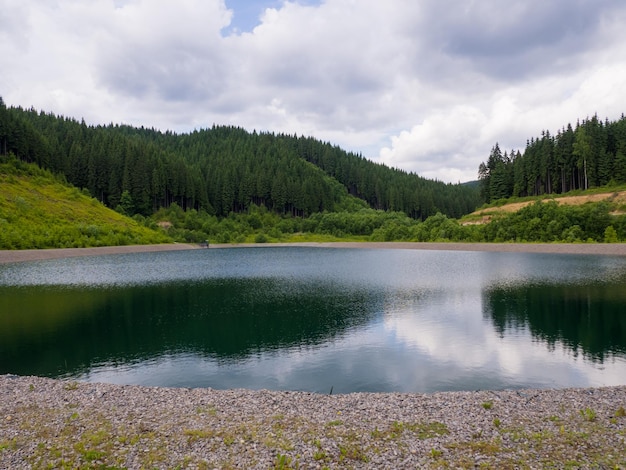 Lago nelle montagne dei Carpazi in una giornata estiva nuvolosa Piccolo lago vuoto nella foresta a Bukovel Ucraina Acqua limpida con spiaggia di ghiaia Paesaggio idilliaco in montagna