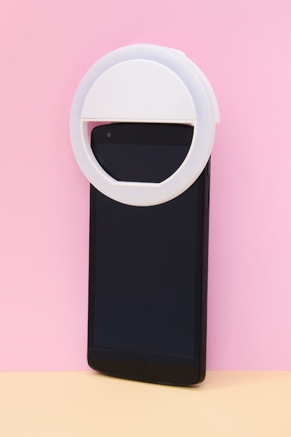 Lampada LED ad anello circolare selfie su smartphone su sfondo giallo rosa. Telefono con fotocamera con luce flash a clip per scattare foto selfie. Dispositivo compatto per blogger e vlogger. Colpo verticale