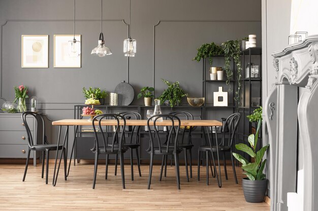 Lampade sopra il tavolo in legno e sedie nere nell'interno grigio della sala da pranzo con piante Foto reale