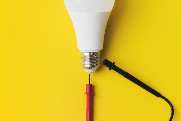 Lampadina a led con sonde multimetro su sfondo giallo. Nuova tecnologia dell'energia