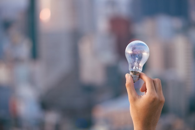 Lampadina sopra le case urbane di tramonto. lampadina trasparente lampada nell'energia solare alternativa dell'uomo nella vita notturna urbana, cittadina, cittadina. Simbolo, concetto di nuova idea creativa di affari. Risparmia energia ecologica