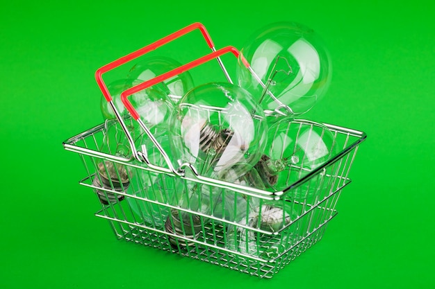 Lampadine con minibasket o carrello su sfondo verde per il concetto di risparmio energetico