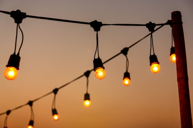 lampadine vintage su filo stringa contro decorazioni tramonto in festa evento matrimonio all&#39;aperto