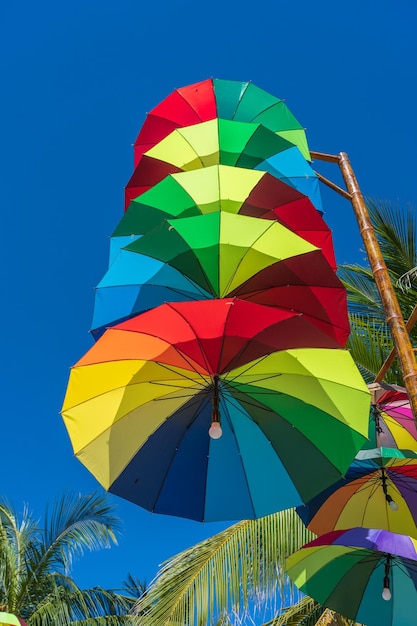 Lampioni decorati con ombrelli colorati appesi su un pilastro in strada contro il cielo blu e la palma da cocco in una giornata di sole