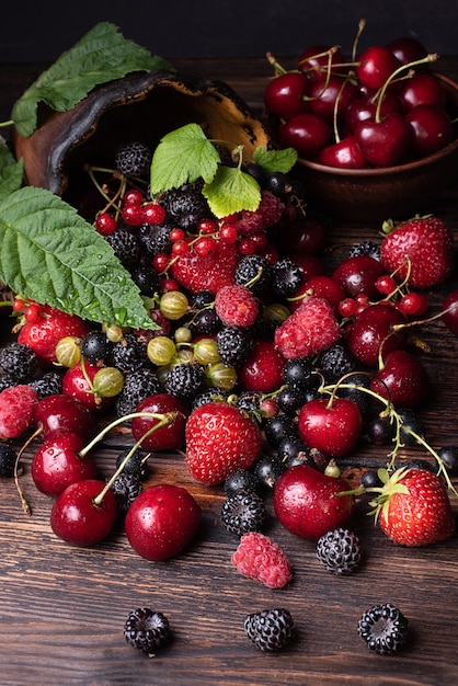 Lamponi, fragole, ciliegie, ribes sparsi da un vaso di argilla su uno sfondo di legno scuro bacche sane, primo piano.