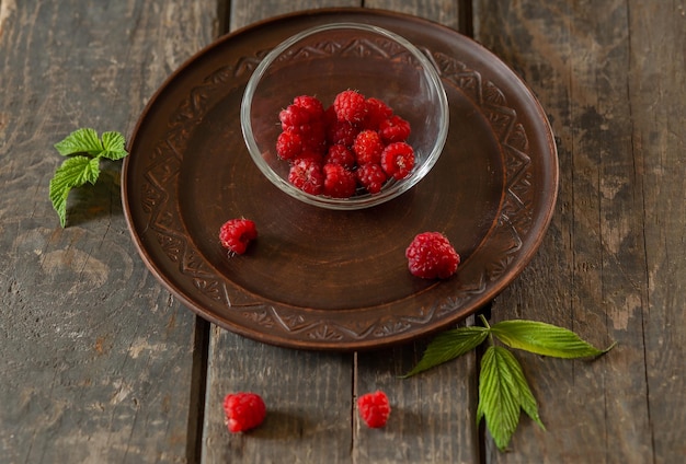 Lamponi in un piattino trasparente su un piatto di ceramica su tavole di legno Frutta estate cibo