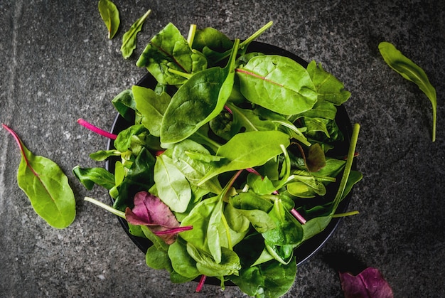 Lanci con le foglie organiche verdi fresche, lattuga degli spinaci del bambino, su una tavola di pietra nera, vista superiore dello spazio della copia