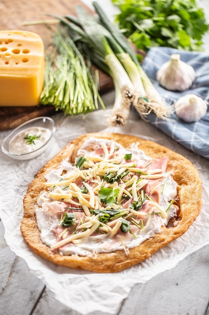 Langos ungherese appena amico servito su carta da forno con panna, formaggio, prosciutto, aglio e cipolla grren.