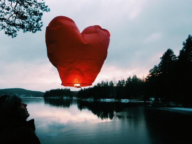 Lanterna di carta illuminata a forma di cuore sopra il lago contro un cielo nuvoloso