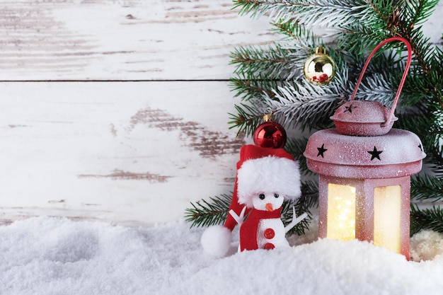 Lanterna di Natale sulla neve con ramo di abete e pupazzo di neve in un cappello di Babbo Natale Biglietto di auguri di Natale