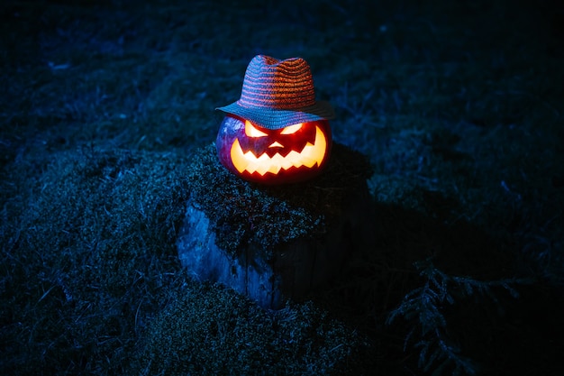 Lanterna di zucca con una terrificante faccia scolpita in un cappello su un concetto di moncone di muschio della vacanza di halloween