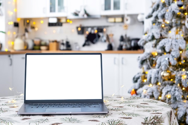 Laptop con uno schermo bianco mock up nella confortevole cucina di Natale decorata in bianco con luci di fata