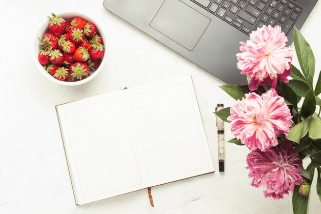 Laptop, diario e piatto bianco con fragole su uno sfondo di pietra chiara. Concetto di lavorare a casa in un'atmosfera accogliente. Vista piana, vista dall'alto