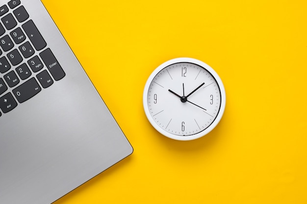 Laptop e sveglia su sfondo giallo. Il tempo corre via. Il concetto di scadenze urgenti sul lavoro e impegni. Vista dall'alto. Lay piatto