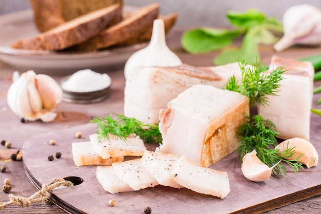 Lardo salato affettato con aglio e aneto su un tagliere su una tavola di legno.