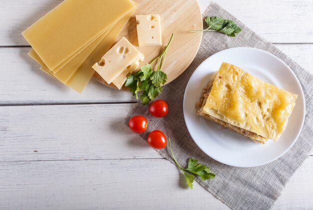 Lasagna con carne macinata e formaggio sulla superficie in legno bianco.