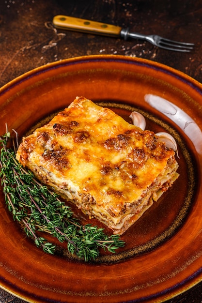 Lasagne italiane con salsa bolognese di pomodoro e carne di manzo tritata su un piatto rustico. Sfondo scuro. Vista dall'alto.