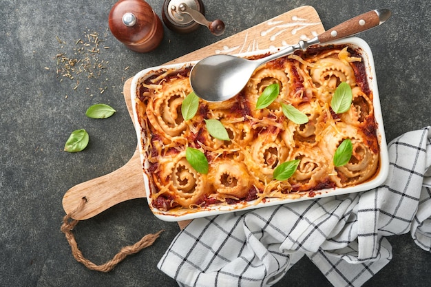 Lasagne Rotolo di pasta di lasagne fatte in casa con salsa di pomodoro crema di formaggio e basilico su padella bianca su pietra ardesia scura o sfondo di cemento Concetto di cucina italiana Vista dall'alto con spazio di copia