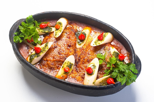 Lasagne servite in una pentola di terracotta con cuori di palma, pesto e peperoncino.