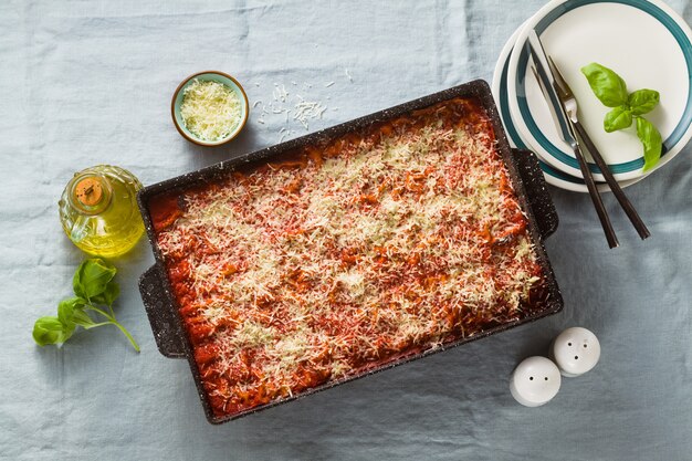 Lasagne vegane con lenticchie e piselli in una teglia su un tavolo con una tovaglia di lino blu.