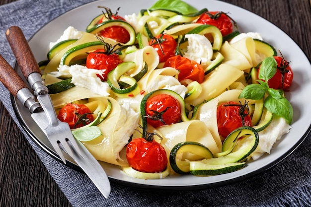 Lasagne vegetariane aperte con zucchine mozzarella pomodori arrosto basilico su un piatto su un tavolo di legno scuro primo piano