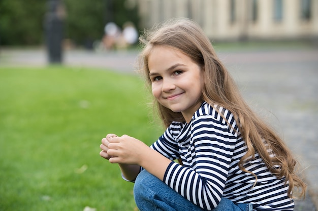 Lascia che il tuo bambino si prenda cura di più Bambino felice seduto sui talloni all'aperto Bambina