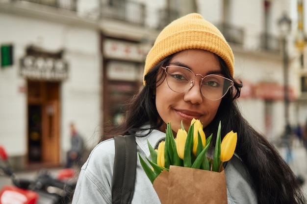 Latina gioiosa che sente l'odore dei tulipani soleggiati sulla strada vibrante