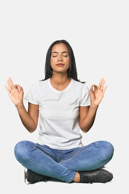 Latina seduta sul pavimento in studio si rilassa dopo una dura giornata di lavoro sta facendo yoga