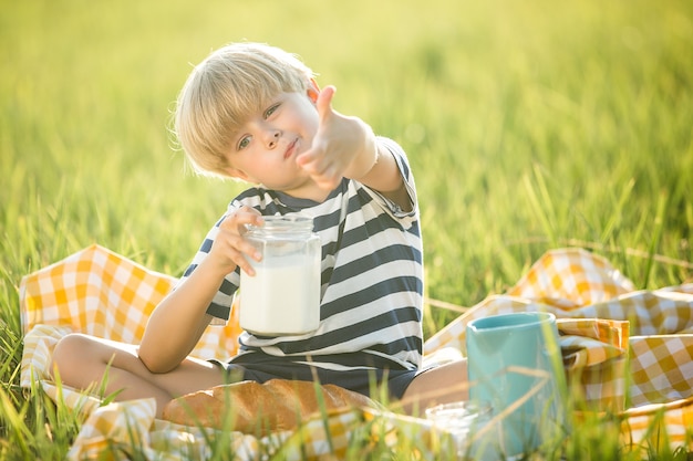 Latte alimentare del bambino sveglio all'aperto. Ragazzo allegro sul picnic