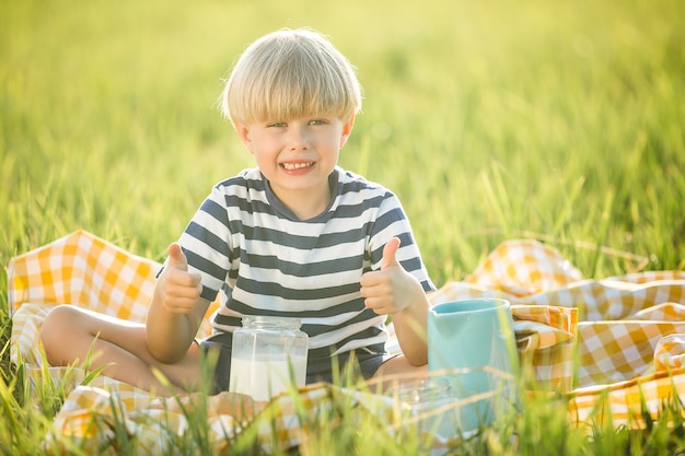 Latte alimentare del bambino sveglio all'aperto. Ragazzo allegro sul picnic