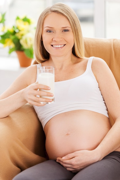 Latte alimentare della donna incinta. Bella donna incinta seduta sulla sedia e con in mano un bicchiere di latte