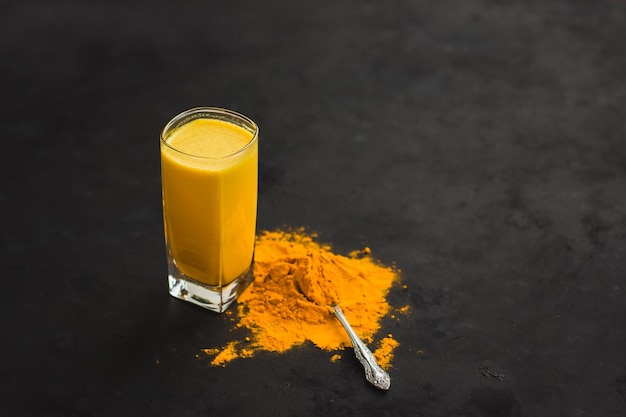 Latte alla curcuma una bevanda salutare calda e lattiginosa dorata su uno sfondo scuro in un bicchiere di vetro