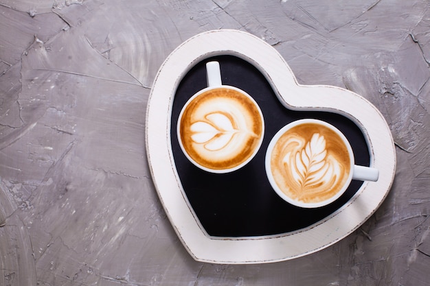 Latte art in due tazze di cappuccino sul vassoio a forma di cuore. Felice mattina di San Valentino coppia
