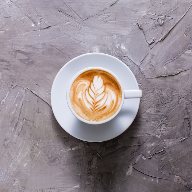 Latte art in tazza di cappuccino. Vista dall'alto su sfondo grigio cemento