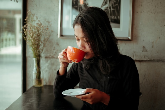 Latte bevente del caffè della donna asiatica nel tono d&#39;annata di colore del caffè