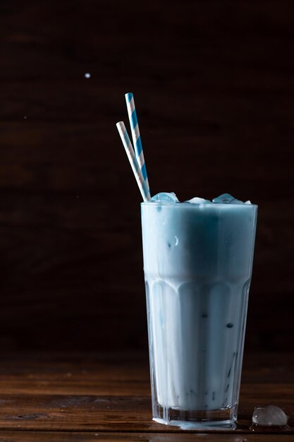 Latte blu in un bicchiere di vetro alto con due cannucce Lo spray sta volando verso l'alto
