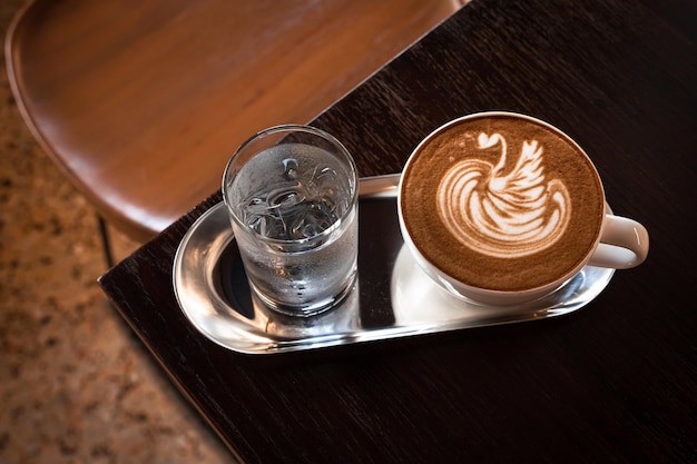 Latte caldo al caffè con schiuma di latte art latte a forma di cigno in tazza sulla scrivania di legno in vista dall'alto Come colazione In una caffetteria al bar durante il concetto di lavoro aziendale