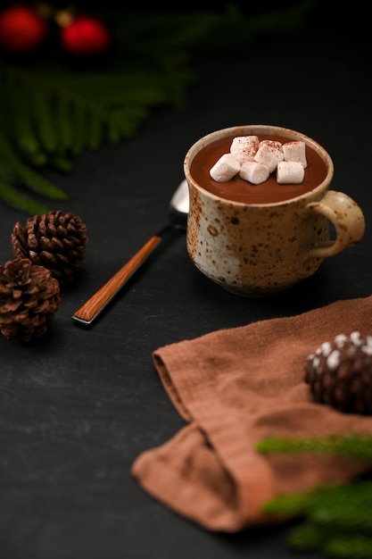 Latte caldo al cioccolato fondente con marshmallow in una tazza di ceramica minimale su sfondo nero tavolo