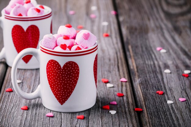 Latte caldo con marshmallow rosa in tazze con cuori su fondo di legno per San Valentino