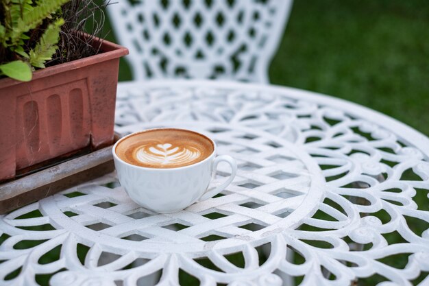 Latte caldo del caffè con schiuma a forma di fiore in tazza bianca sulla retro tavola