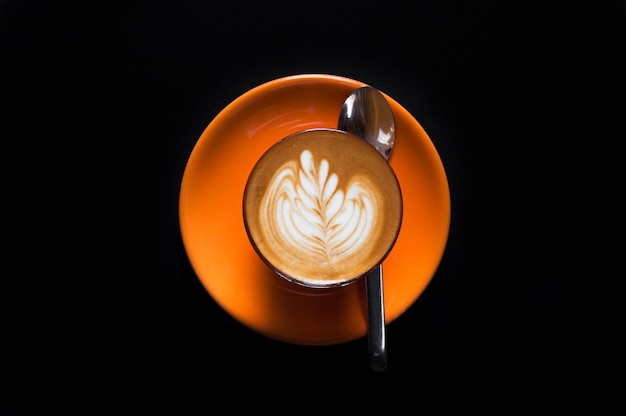 Latte caldo in tazza arancione con motivo floreale in schiuma su sfondo scuro